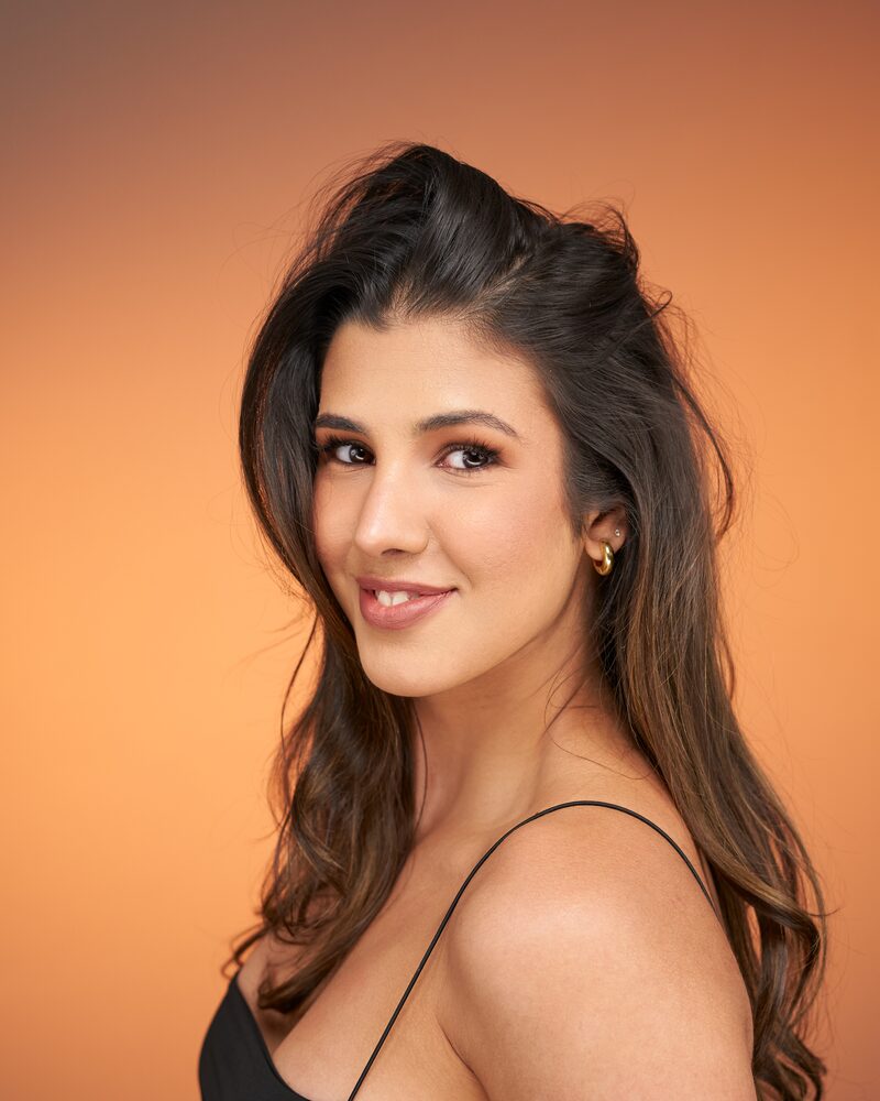 Jeannet Garcia headshot — black strappy top, warm orange backdrop, soft smile