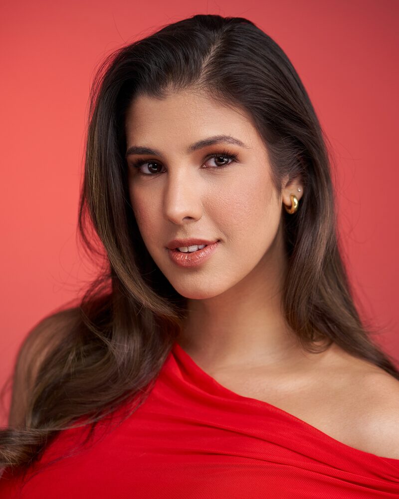 Jeannet Garcia formal portrait — red one-shoulder dress, red backdrop, soft smile
